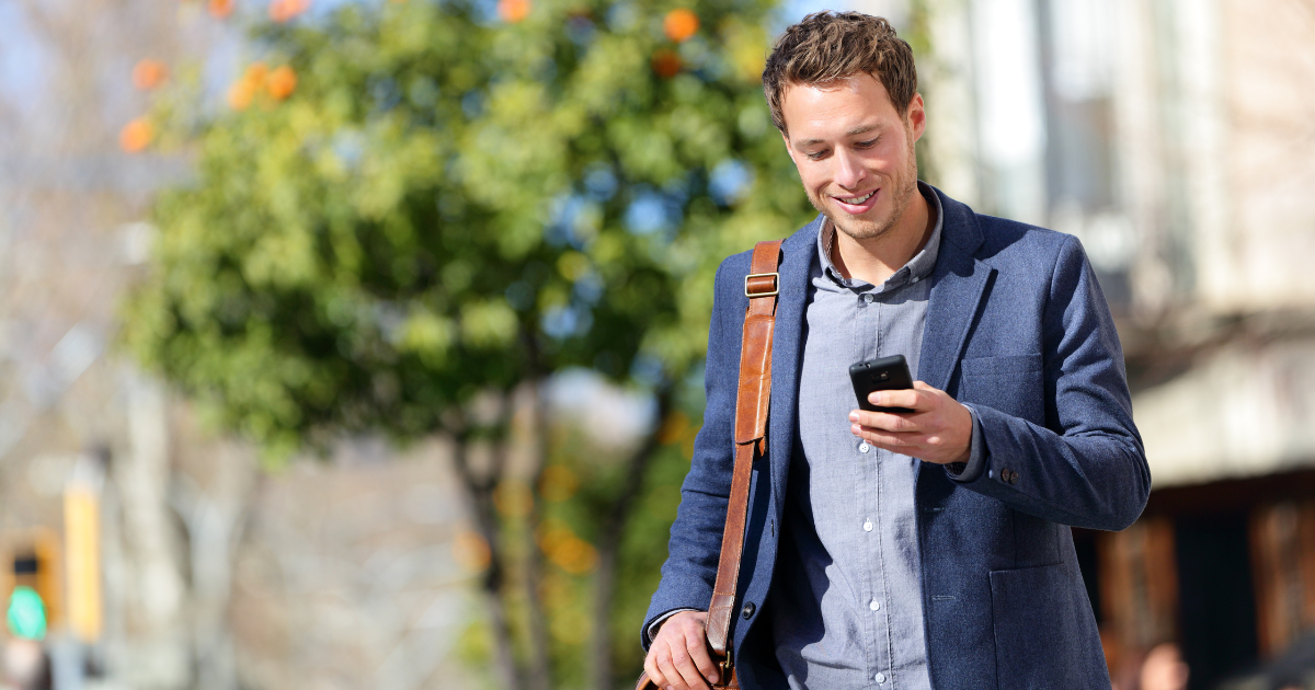 Man walking in a blue suit looking at his cellphone and smiling